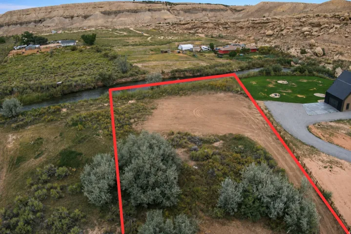 Expansive parcel featuring a natural watercourse, bordered by a gravel driveway, and surrounded by distant natural rock formations