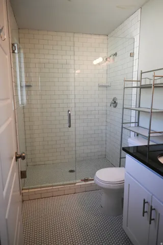 Glass-enclosed shower with subway tile surround, penny tile shower pan, and chrome fixtures