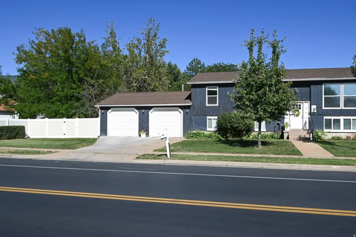 Two-car garage, dark exterior siding, white trim windows, concrete driveway, and a front walkway