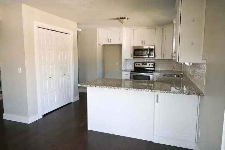Kitchen with white cabinetry, granite countertops, stainless steel appliances, subway tile backsplash, and dark wood-finish flooring
