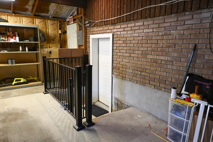 Brick wall construction with a white panel door, concrete flooring, and metal railing