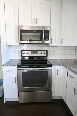 White shaker-style cabinetry with brushed nickel hardware, stainless steel appliances, subway tile backsplash, and speckled countertops