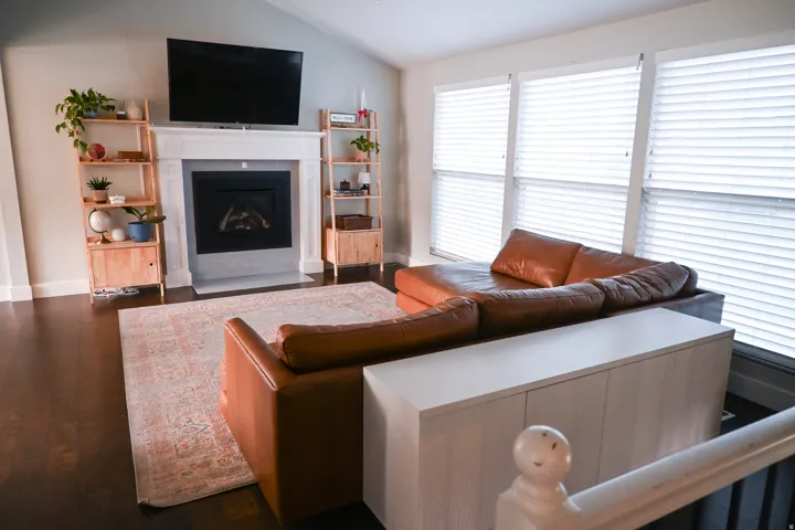 Vaulted ceiling, dark wood-finish flooring, white mantel, built-in fireplace, and three large windows with blinds