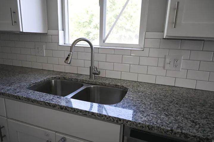 Granite-finish countertops, stainless steel double basin sink, pull-down spray faucet, white subway tile backsplash, and shaker-style cabinetry