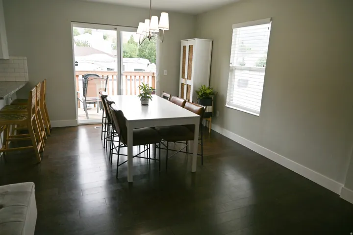 Dark wood-finish flooring, sliding glass door, single hung window with blinds, white subway tile backsplash, and overhead chandelier
