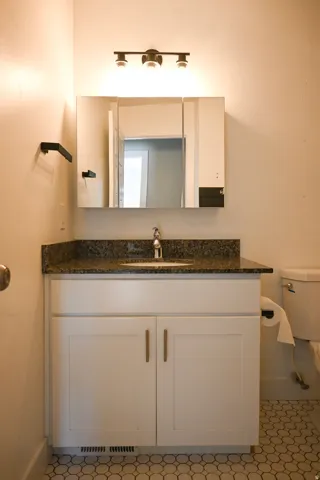 White vanity with shaker-style cabinet doors, granite-style countertop, and drop-in sink