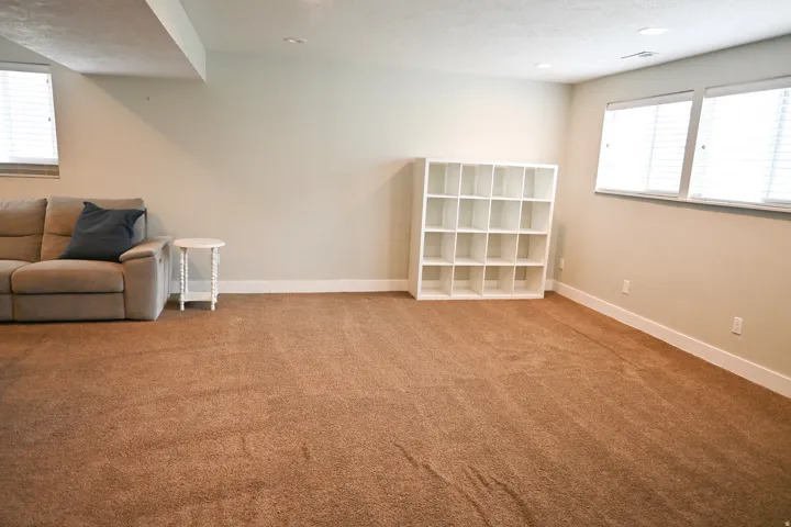 Recessed lighting illuminates the carpeted living area with multiple windows