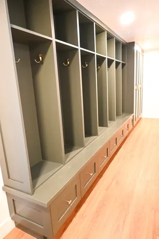 Built-in storage system featuring individual cubbies, integrated bench seating, multiple storage drawers with gold-tone hardware, and wood-finish flooring