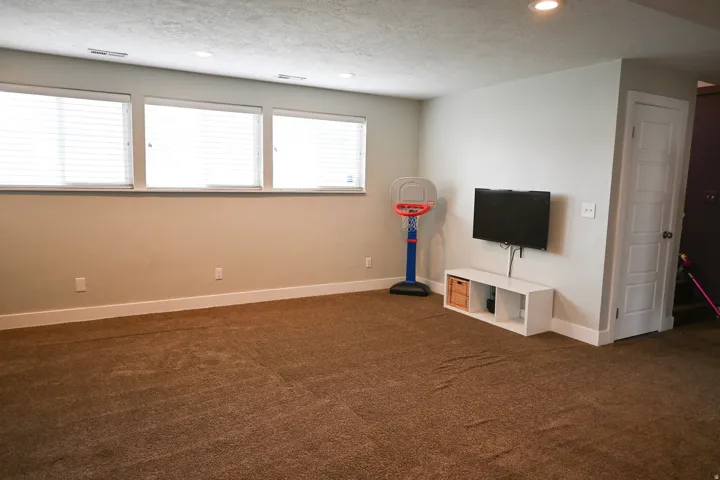 Recessed lighting, wall-mounted television, built-in shelving, carpet flooring, and three windows with blinds