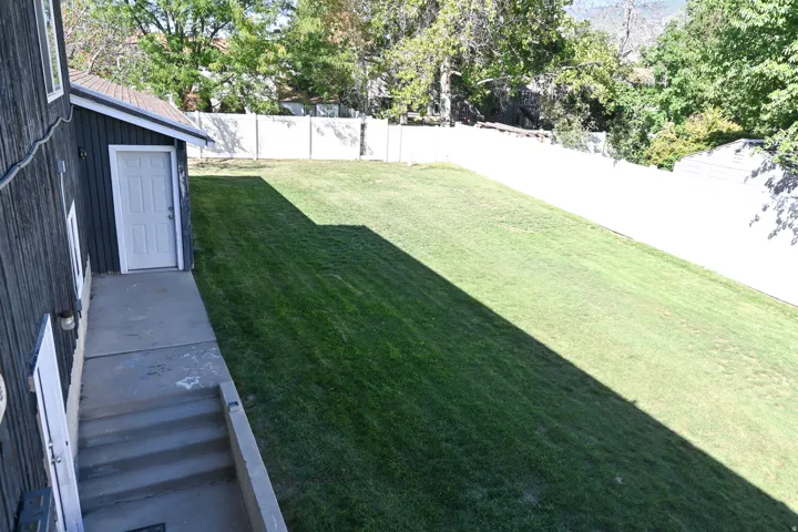 Expansive grassy yard with a white privacy fence and mature perimeter trees