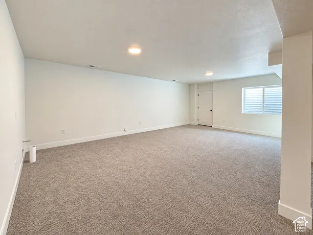 Spacious carpeted room featuring white painted walls, recessed lighting, a white door with black hardware, and a window with horizontal blinds