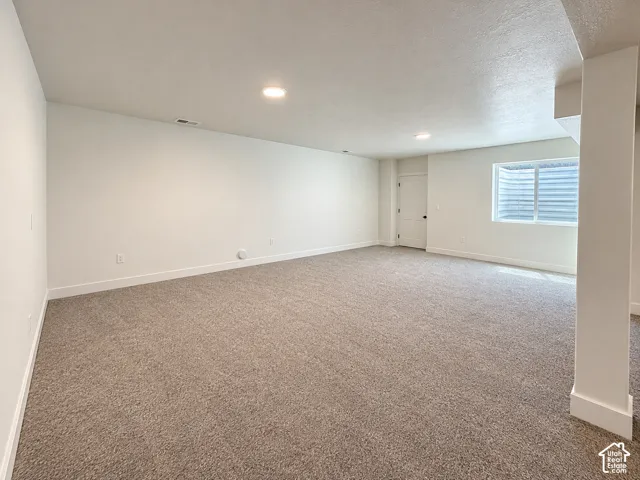 Spacious room featuring neutral carpet flooring, recessed lighting, and a white interior door