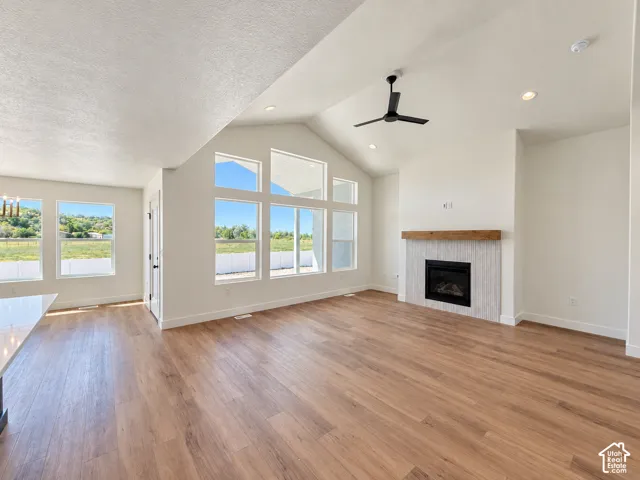 Vaulted ceiling with a contemporary ceiling fan, wood-finish flooring, a fireplace with a wood mantle, and large picture windows