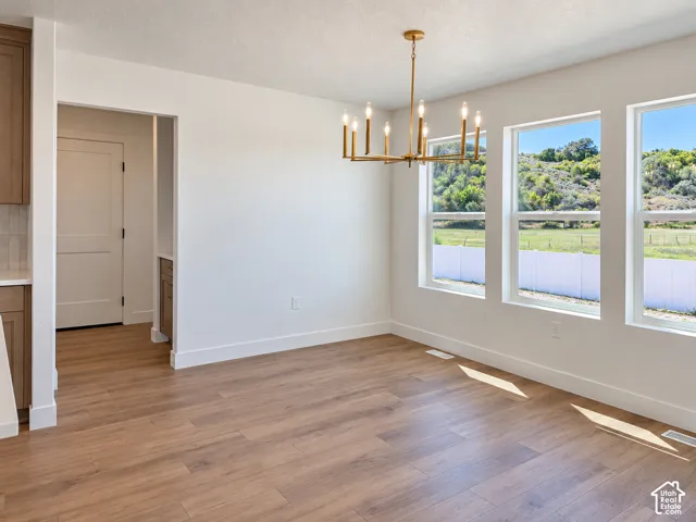 Wood-finish flooring, multiple windows, gold-tone chandelier, white trim, and light-toned walls