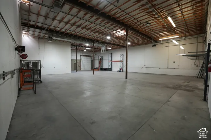 Expansive open floor plan with concrete flooring, exposed wood beam ceiling, and fluorescent lighting