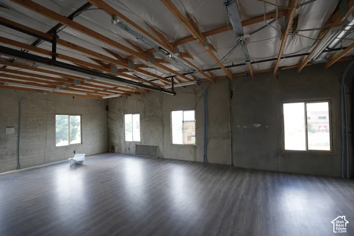 Open-concept interior featuring exposed ceiling joists, wood-finish flooring, multiple windows, and surface-mounted lighting