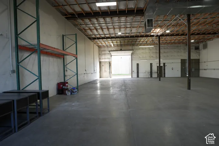 Expansive concrete flooring throughout, exposed wood beam ceiling, multiple interior doorways, and an overhead door