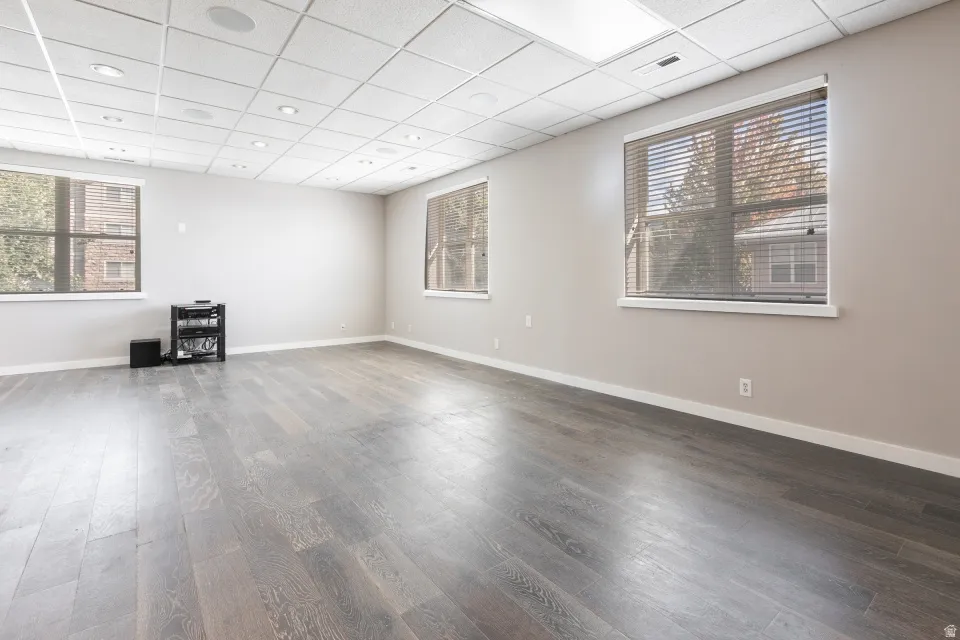 Recessed ceiling lighting, wood-finish flooring, multiple windows with blinds, and a suspended acoustic tile ceiling