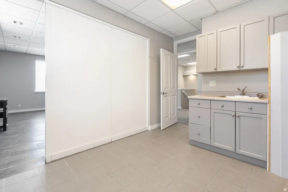 Built-in cabinetry with a light countertop and single-basin sink, tile flooring, and a drop ceiling with recessed lighting