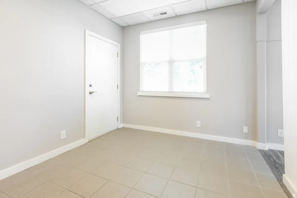 Neutral gray wall finish, white trim, tiled flooring, white door with brushed nickel hardware, and a window with blinds