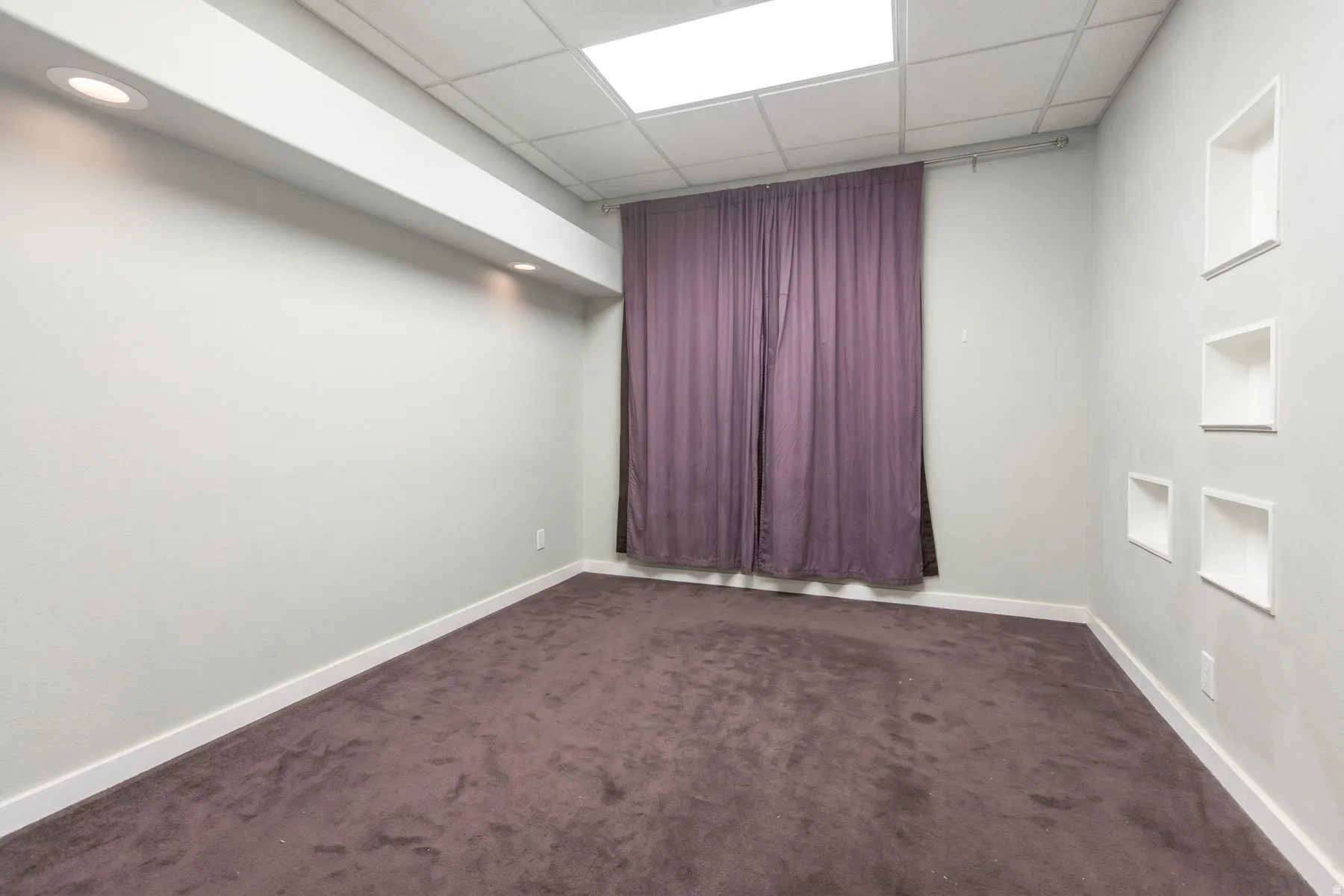 Recessed ceiling lighting, dropped grid ceiling, wall-mounted display niches, full-height window treatment, and broadloom carpeting