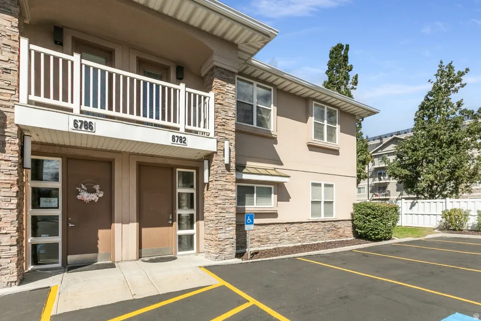 Stucco exterior with stone veneer accents, multi-pane windows, and an upper-level balcony with white railings