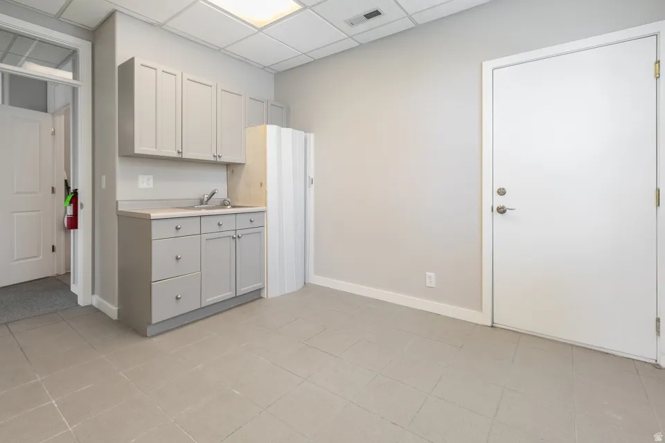 Light gray cabinetry with a stainless steel sink, under-cabinet storage, and tile flooring