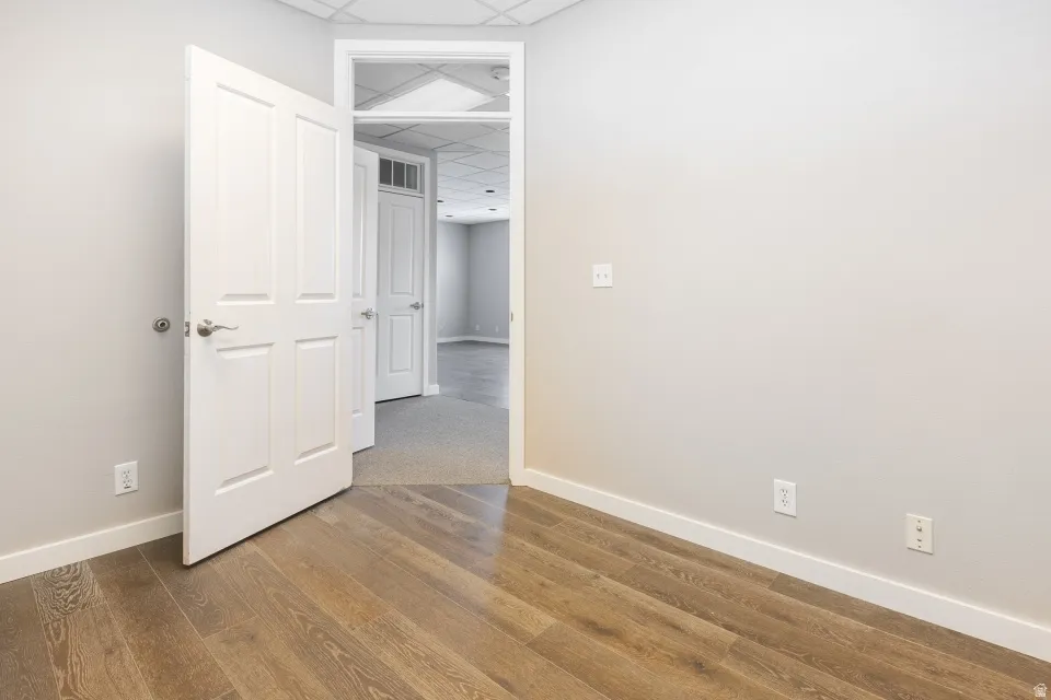 Wood-finish flooring, light gray walls, white trim, and a white paneled door with a brushed nickel handle