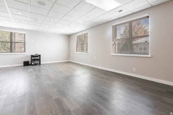 Recessed ceiling lighting, wood-finish flooring, multiple windows with blinds, and a suspended acoustic tile ceiling