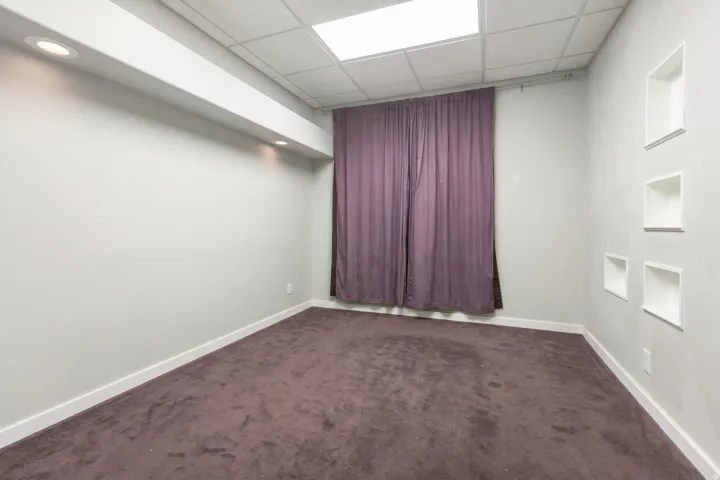 Recessed ceiling lighting, dropped grid ceiling, wall-mounted display niches, full-height window treatment, and broadloom carpeting