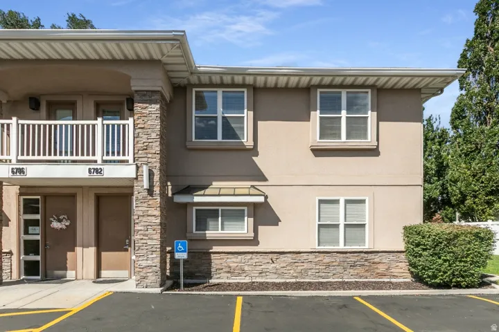 Multi-level stucco exterior with stone veneer accents, white frame windows, and an upper-level balcony with white railings