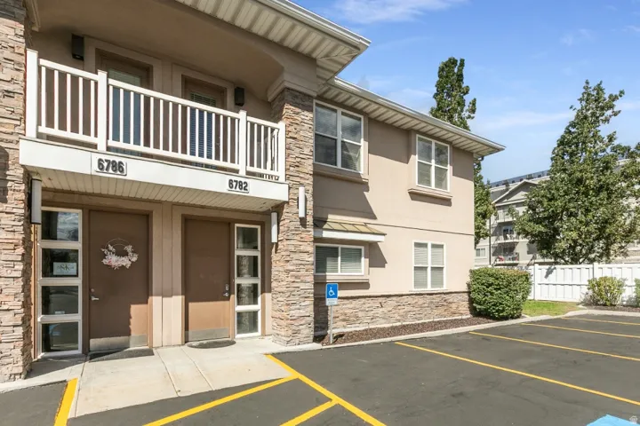 Stucco exterior with stone veneer accents, multi-pane windows, and an upper-level balcony with white railings
