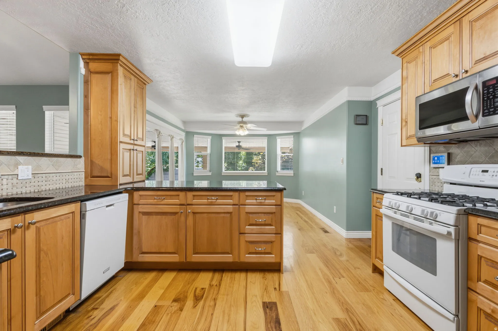 Kitchen featuring wood cabinetry, stainless steel microwave, gas range, dishwasher, and wood-finish flooring