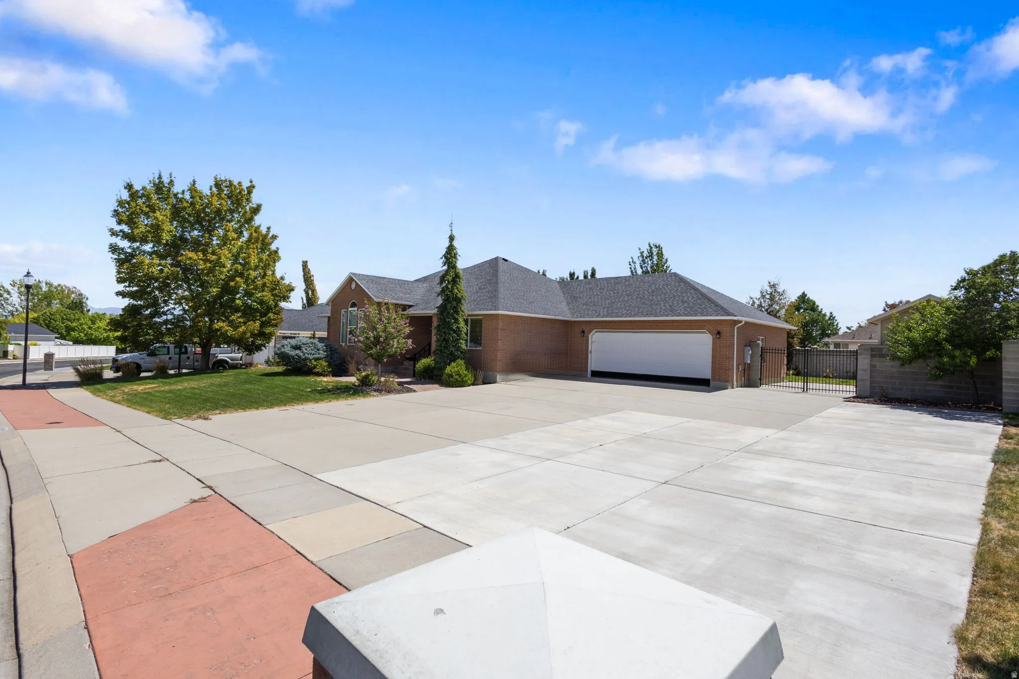 Brick exterior, dark shingle roof, expansive paved driveway, integrated garage, and a gated side entrance