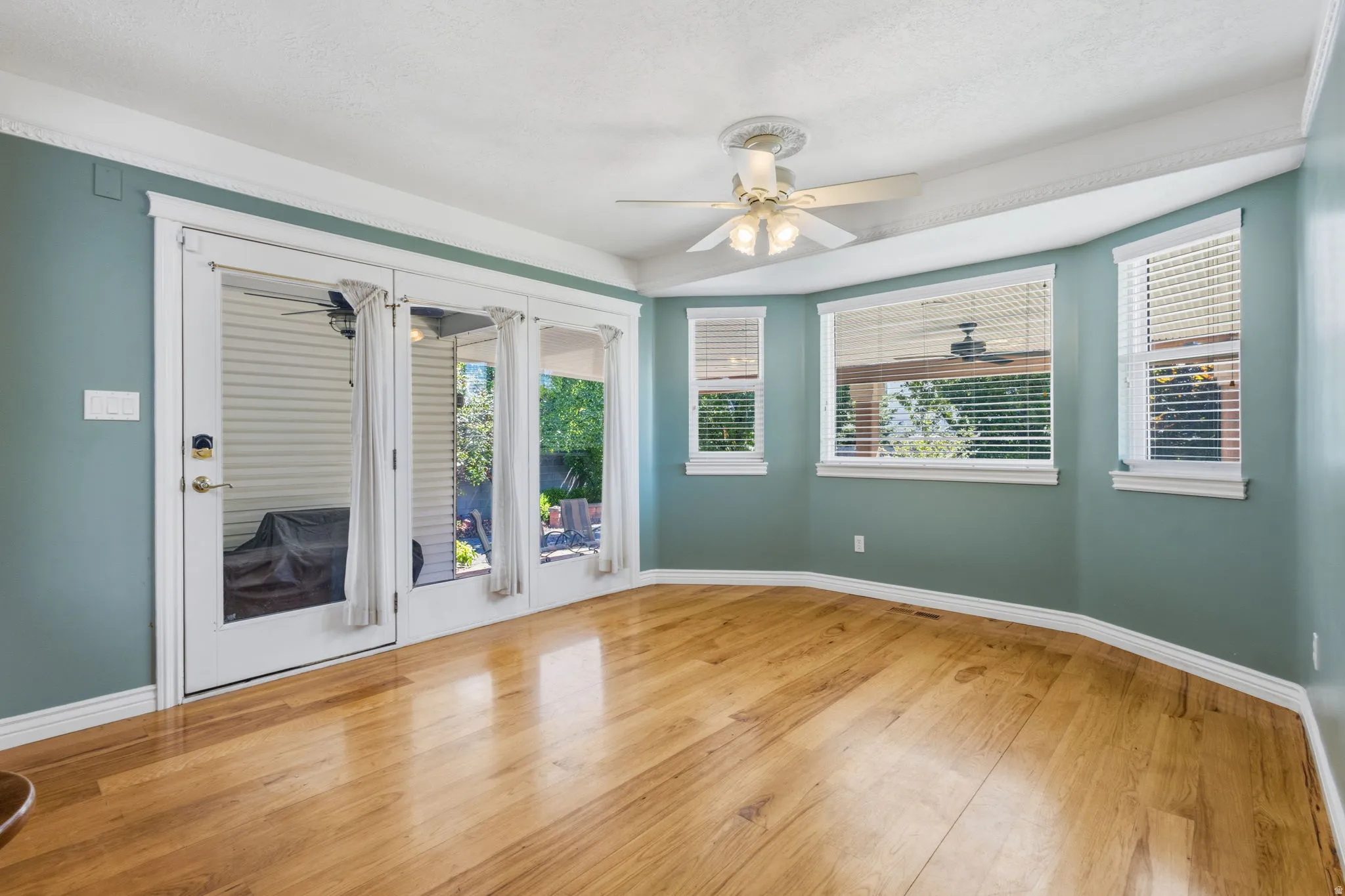 Wood-finish flooring, multiple windows with blinds, ceiling fan with light fixture, and crown molding