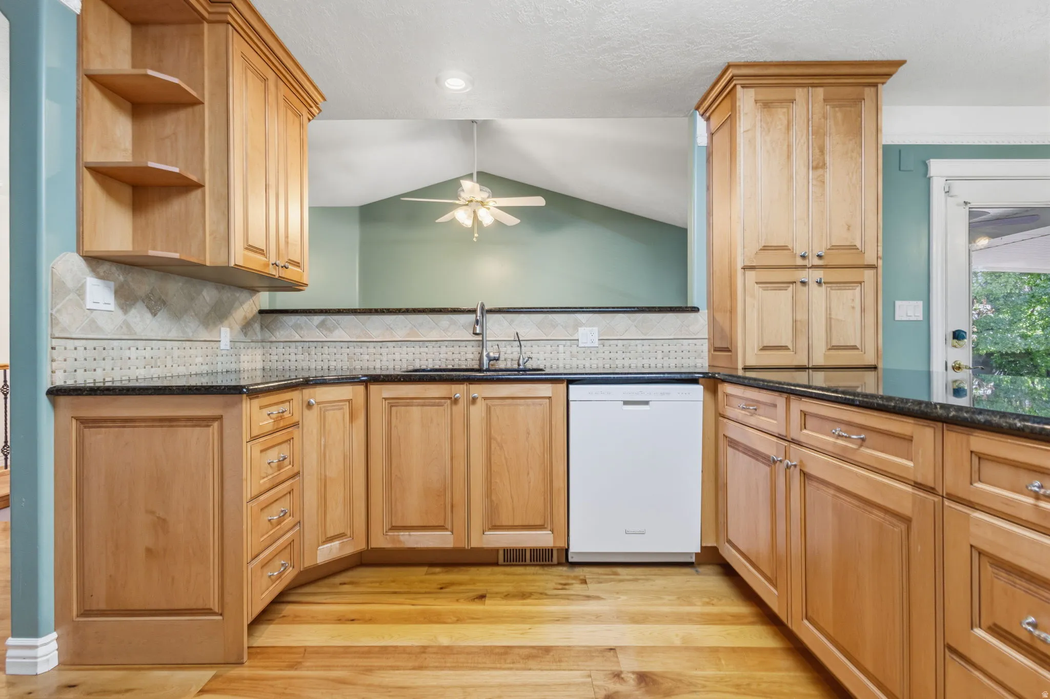 Wood-finish flooring, light wood cabinetry, stone countertops, integrated sink, and white dishwasher