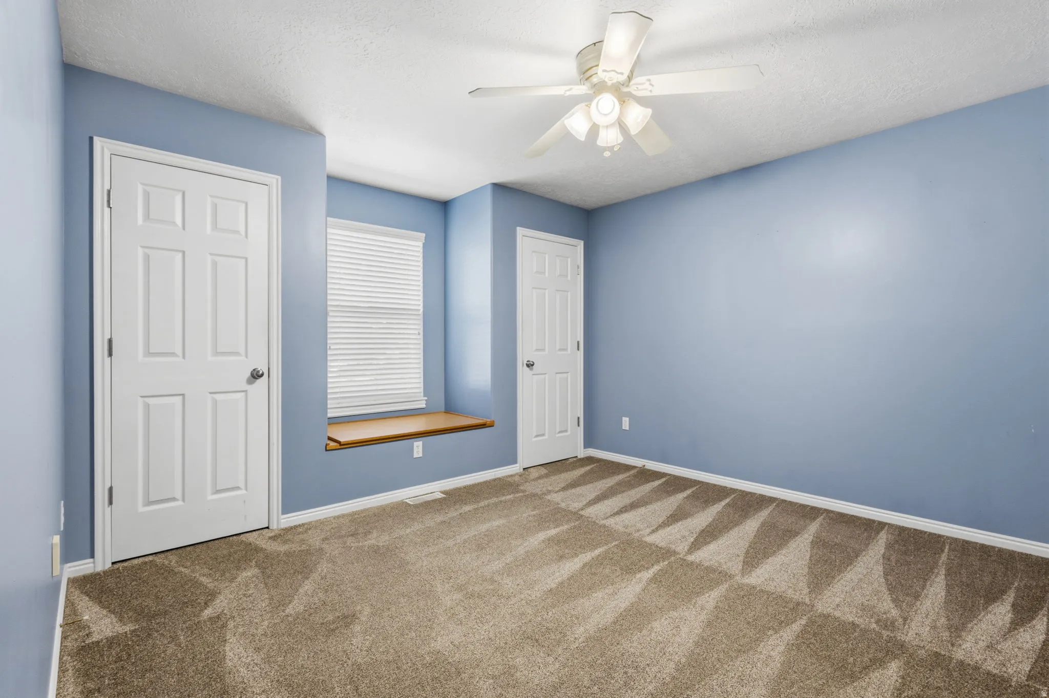 Window with wood-finish sill, ceiling fan, textured ceiling, and patterned carpet flooring