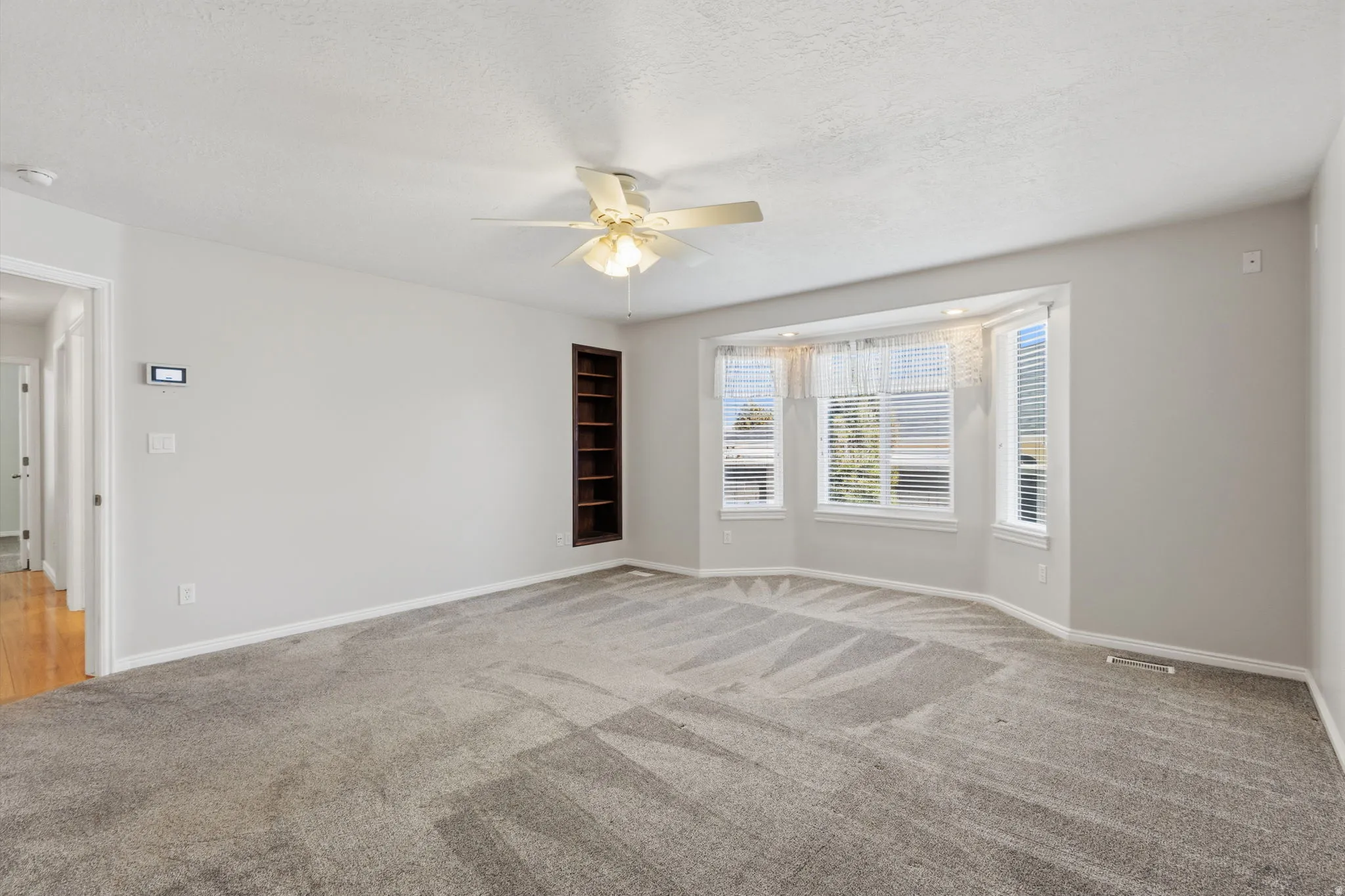Recessed bay window, built-in shelving, ceiling fan, and light-toned carpeting