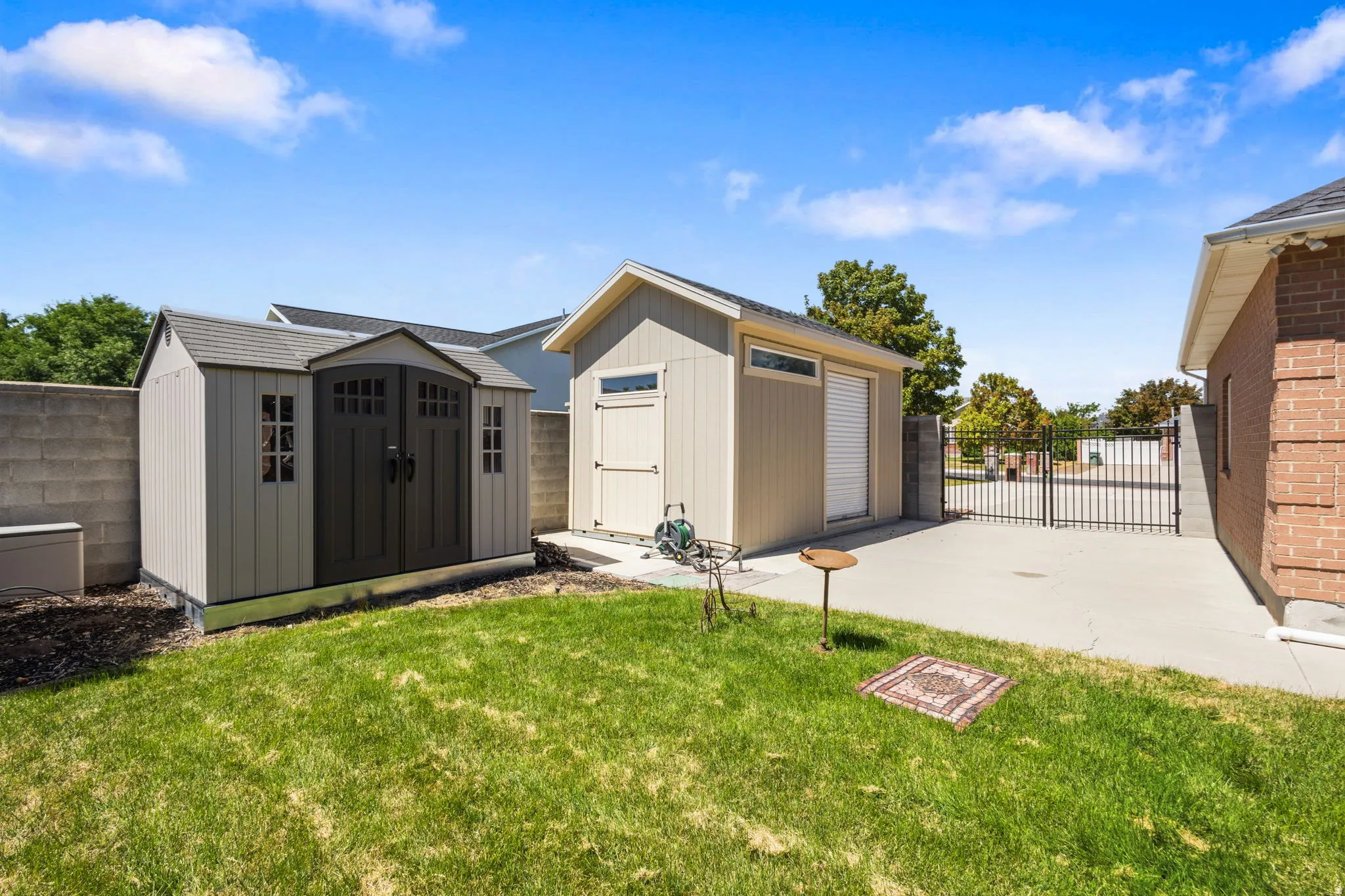 Manicured lawn, two detached storage sheds, concrete patio, and a black metal gate