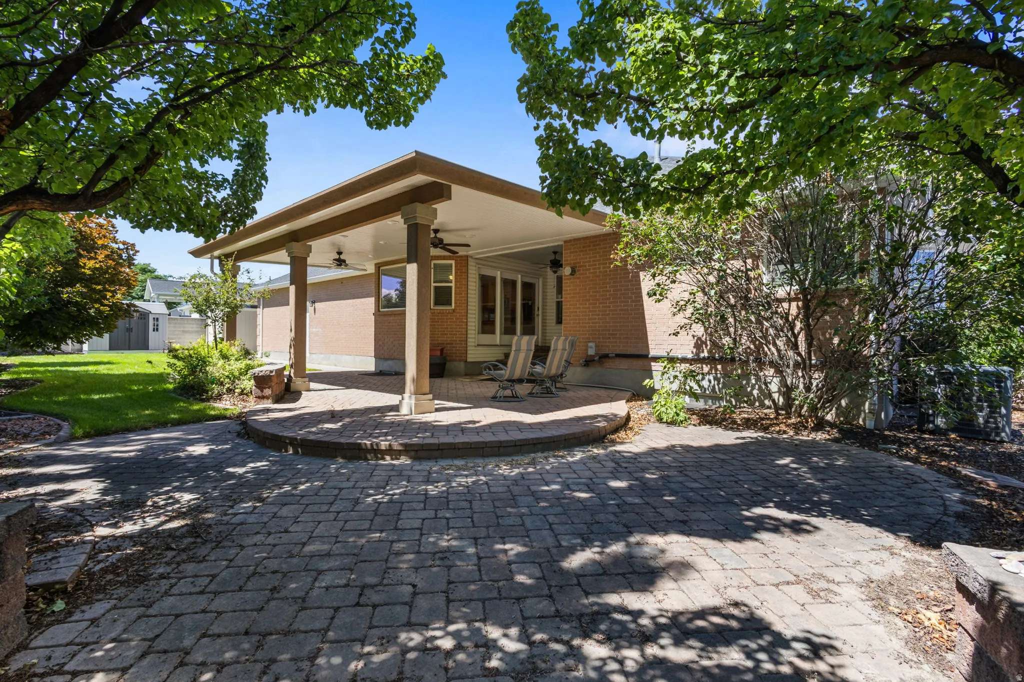 Brick paver patio with a covered outdoor area, ceiling fans, and a grass lawn