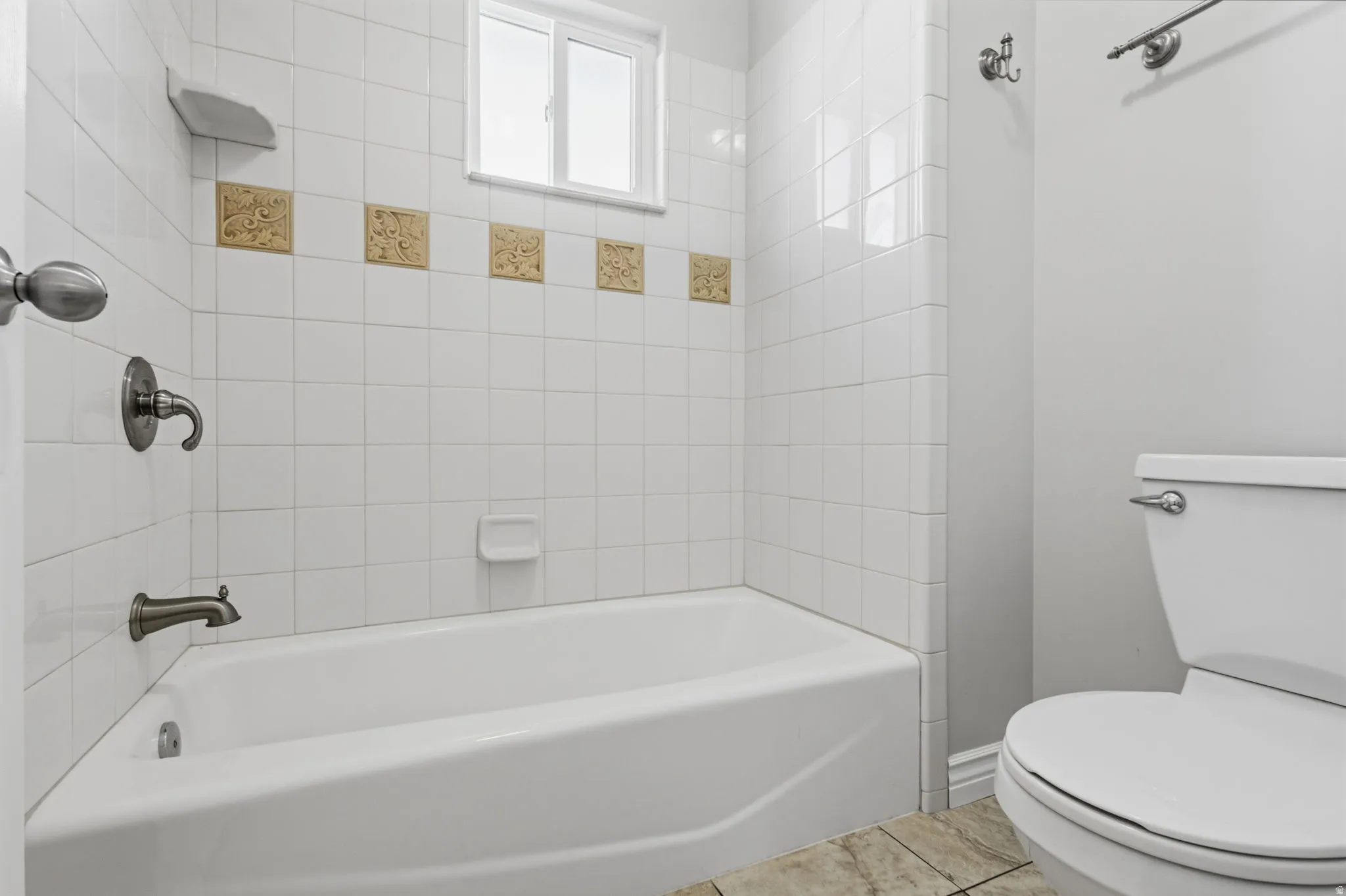 Bathtub with white tile surround, decorative accent tiles, and a window