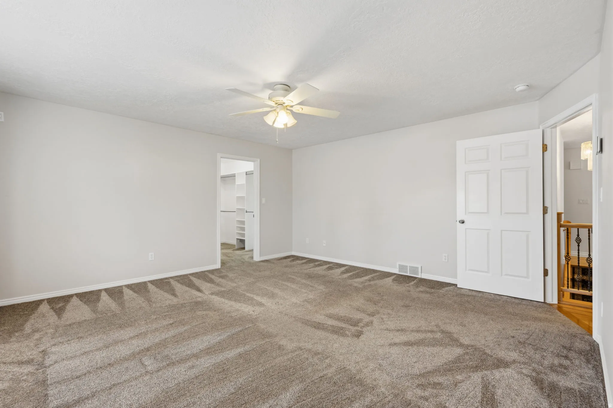Wall-to-wall carpeting in a neutral tone, ceiling fan with integrated lighting, and a closet with built-in shelving