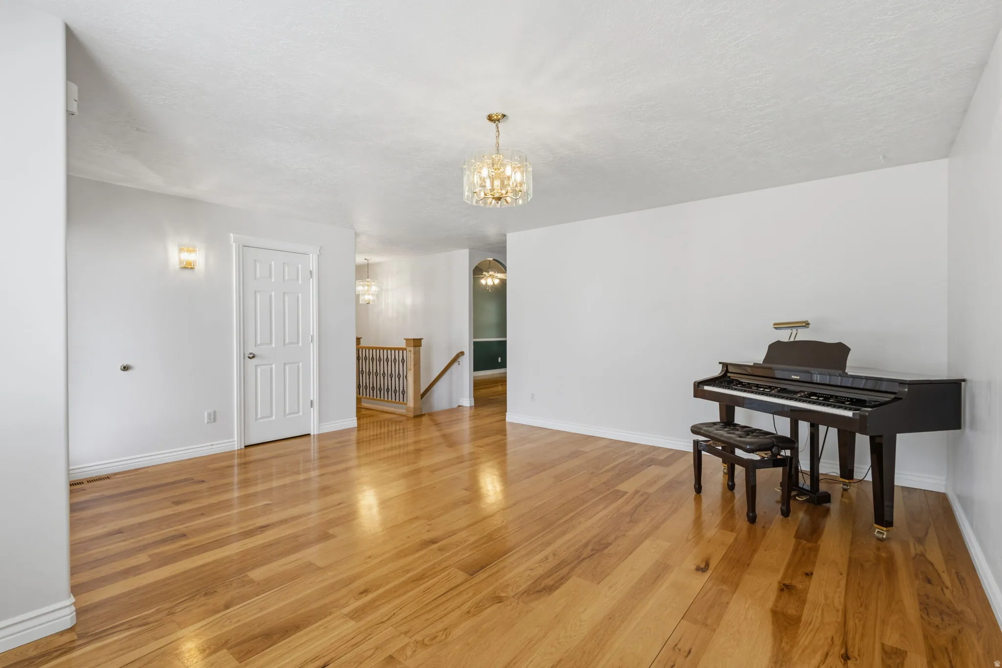 Hardwood flooring, crystal chandelier, wall sconces, white paneled door, and open staircase with wood handrail