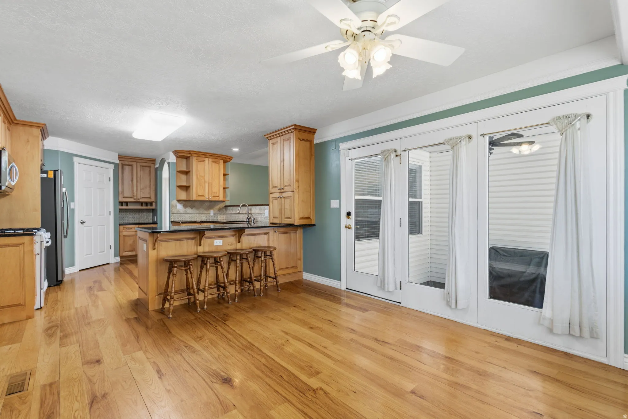 Wood-finish flooring, kitchen island with seating, natural wood cabinetry, pendant lighting, and ceiling fan