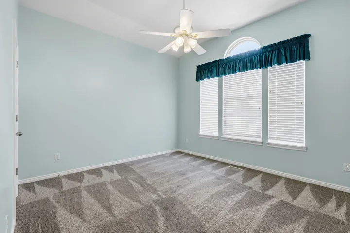 Vaulted ceiling, ceiling fan, three windows with blinds, arched transom window, and patterned carpeting