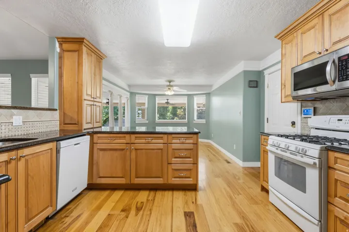 Kitchen featuring wood cabinetry, stainless steel microwave, gas range, dishwasher, and wood-finish flooring