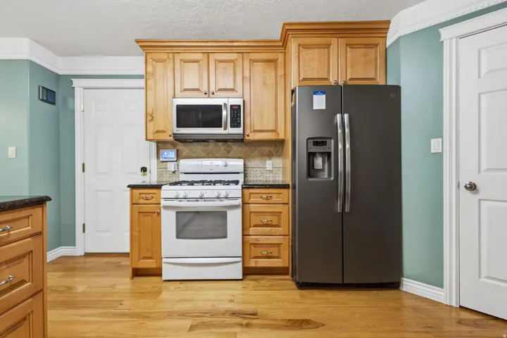 Kitchen featuring wood-finish flooring, natural wood cabinetry, dark countertops, a tile backsplash, and stainless steel appliances