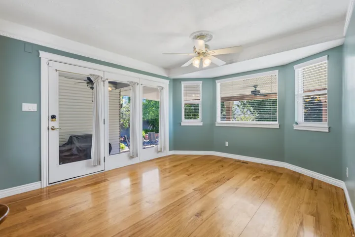 Wood-finish flooring, multiple windows with blinds, ceiling fan with light fixture, and crown molding