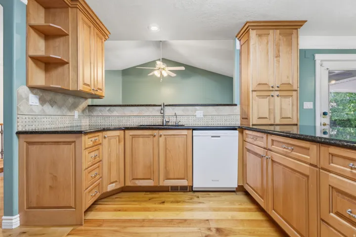 Wood-finish flooring, light wood cabinetry, stone countertops, integrated sink, and white dishwasher