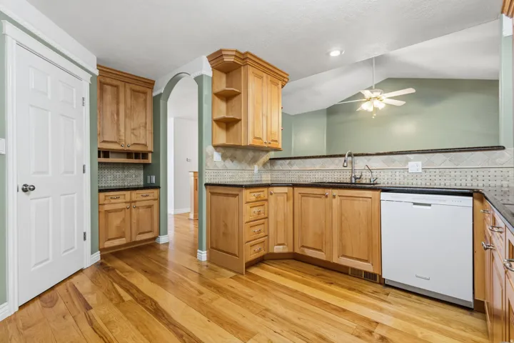 Wood-finish flooring with natural wood cabinetry, dark countertops, and a full tile backsplash